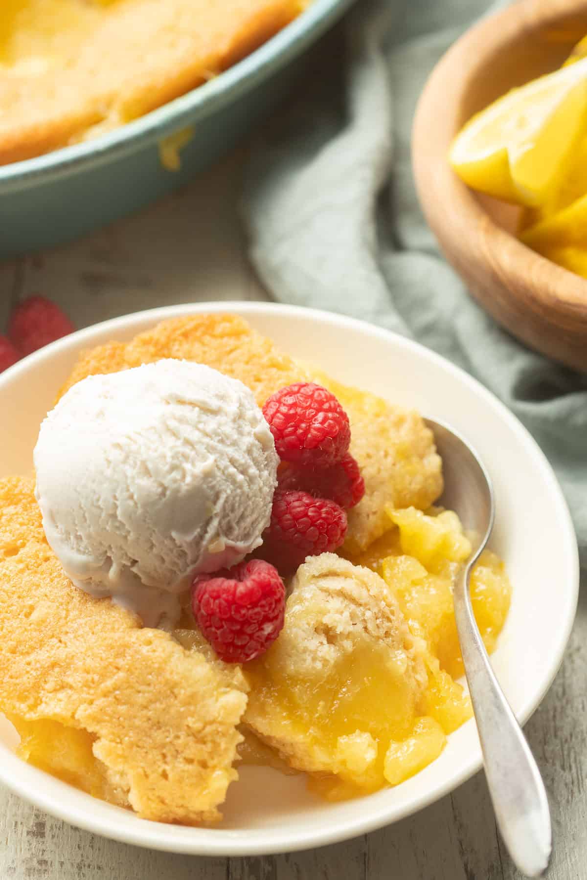 Bowl of Lemon Cobbler with baking dish and bowl of lemons in the background.