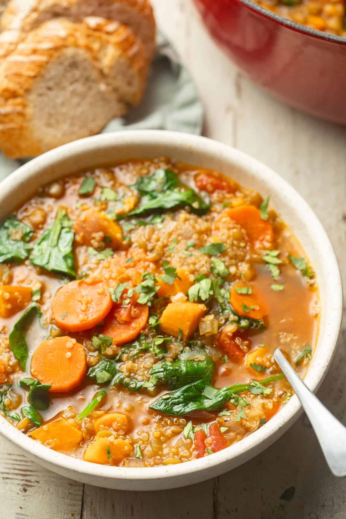Bowl of Quinoa Soup with a pot and loaf of bread in the background.