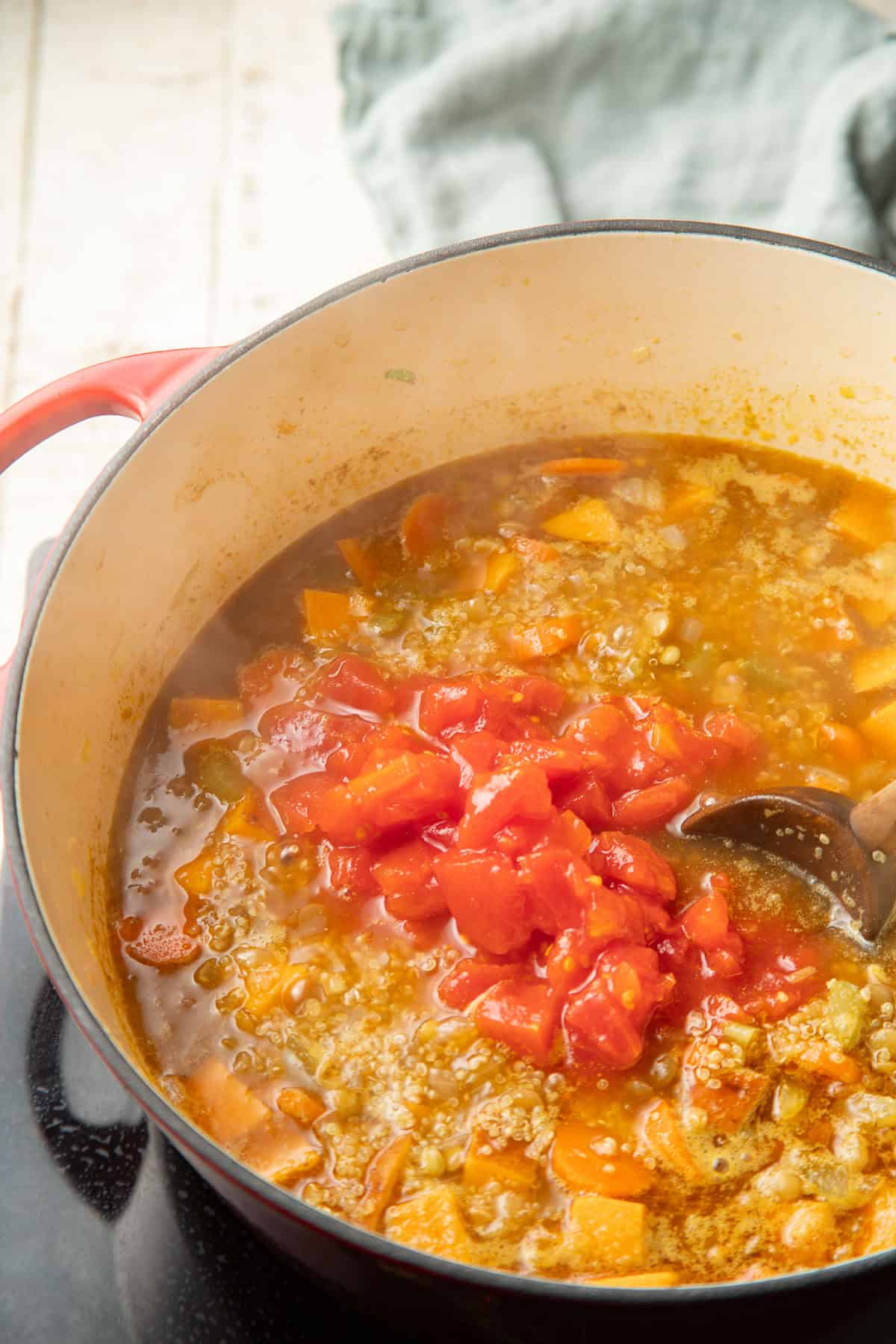 Tomatoes being stirred into a pot of soup.