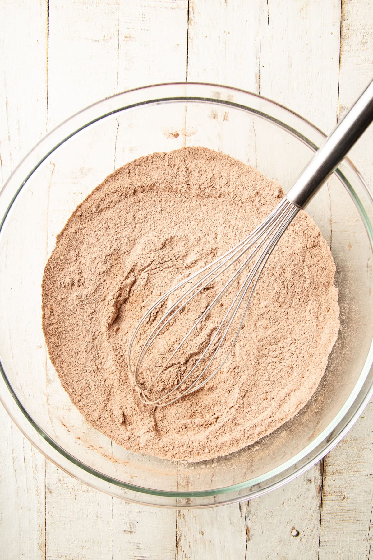 Dry ingredients for chocolate cake in a mixing bowl with wire whisk.
