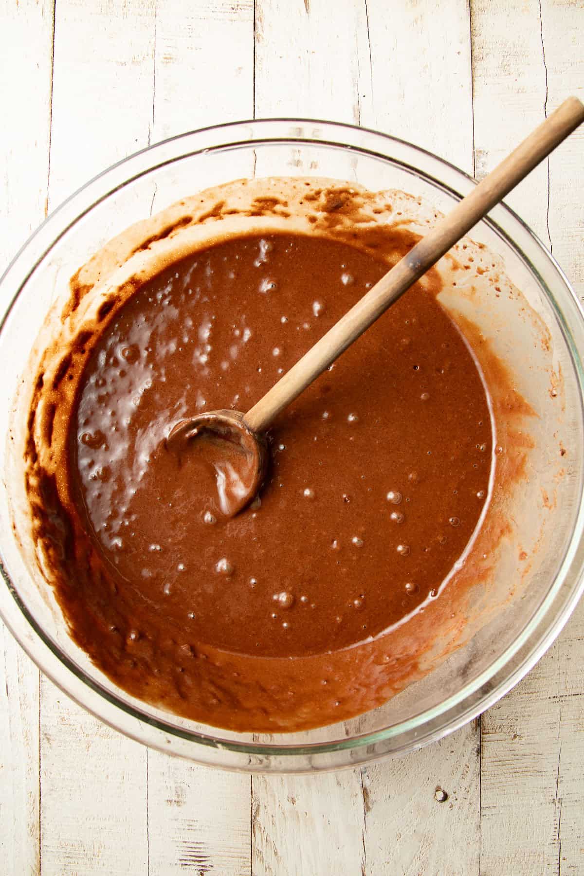 Chocolate cake batter in a mixing bowl with wooden spoon.