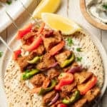 White wooden surface set with Vegan Souvlaki on a pita and bowl of tzatziki.