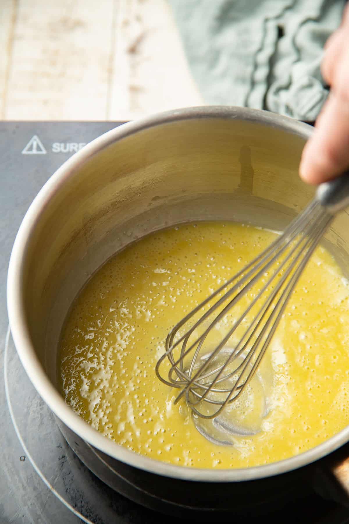 Hand whisking simmering mixture of vegan butter and flour in a saucepan.