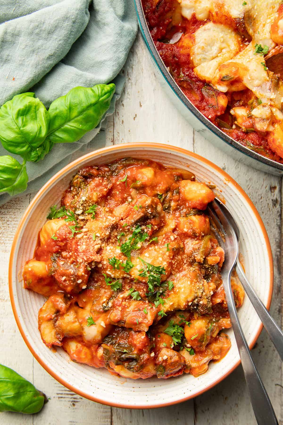 White wooden surface set with baking dish and bowl of Vegan Gnocchi Bake.