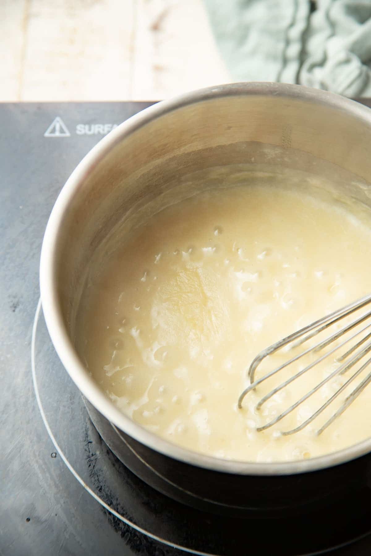 Bechamel sauce simmering in a saucepan with wire whisk.