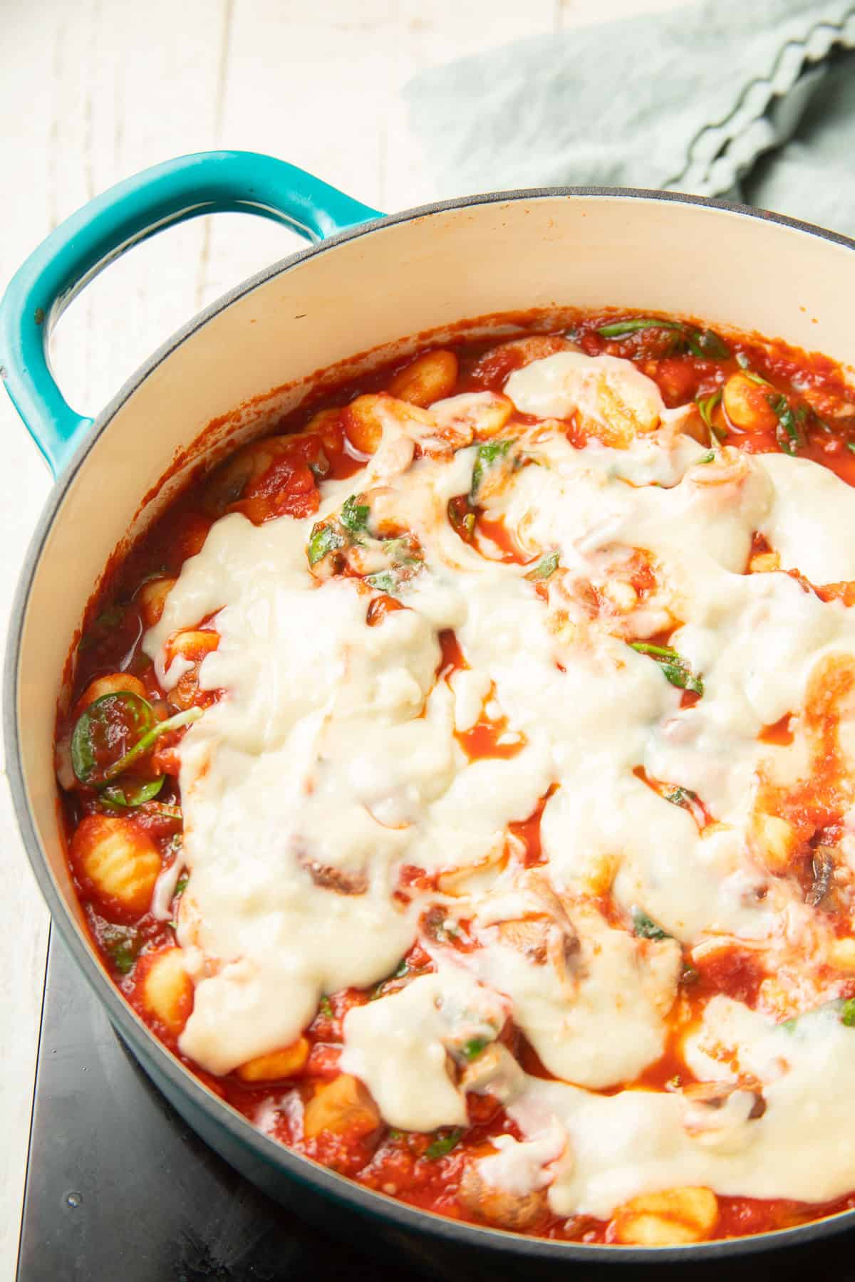 Baking dish of gnocchi, spinach, and mushrooms in tomato sauce, with bechamel on top.
