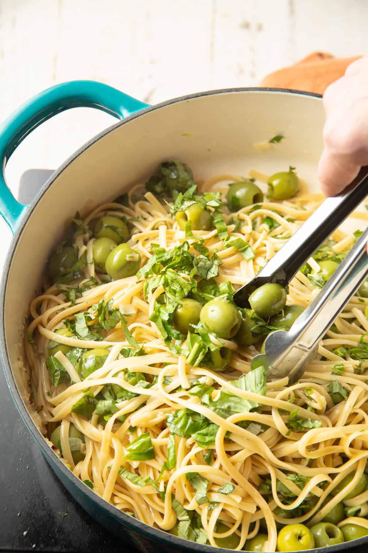 Tongs tossing Green Olive Pasta in a pot.