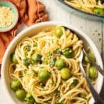 White wooden surface set with pot and bowl of Green Olive Pasta.