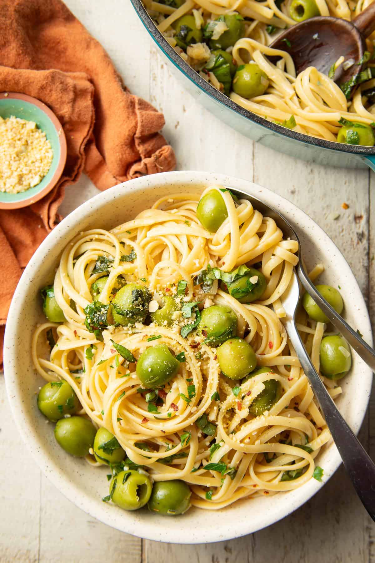 White wooden surface set with pot and bowl of Green Olive Pasta.