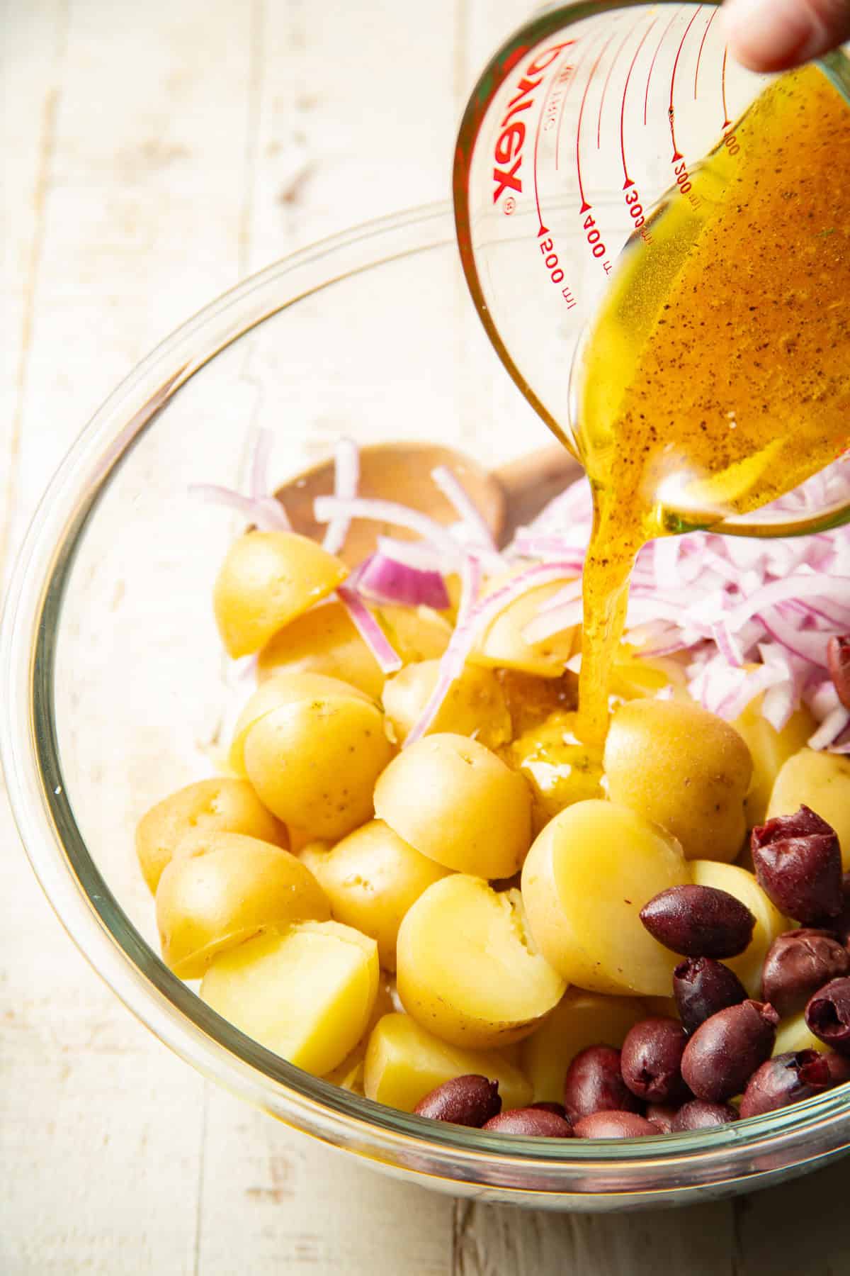 Dressing being poured over Mediterranean Potato Salad in a bowl.