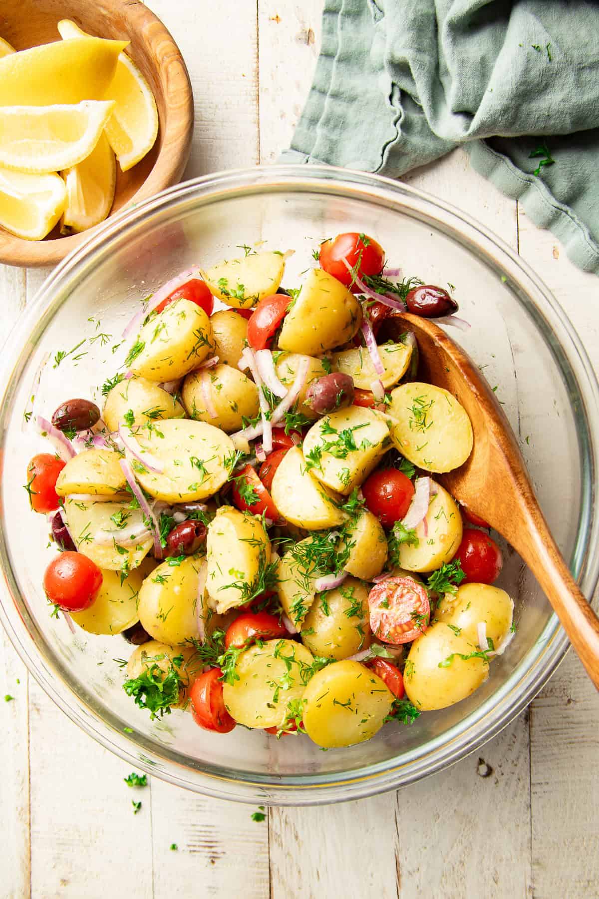 White wooden surface set with bowl of Mediterranean Potato Salad and bowl of lemons.