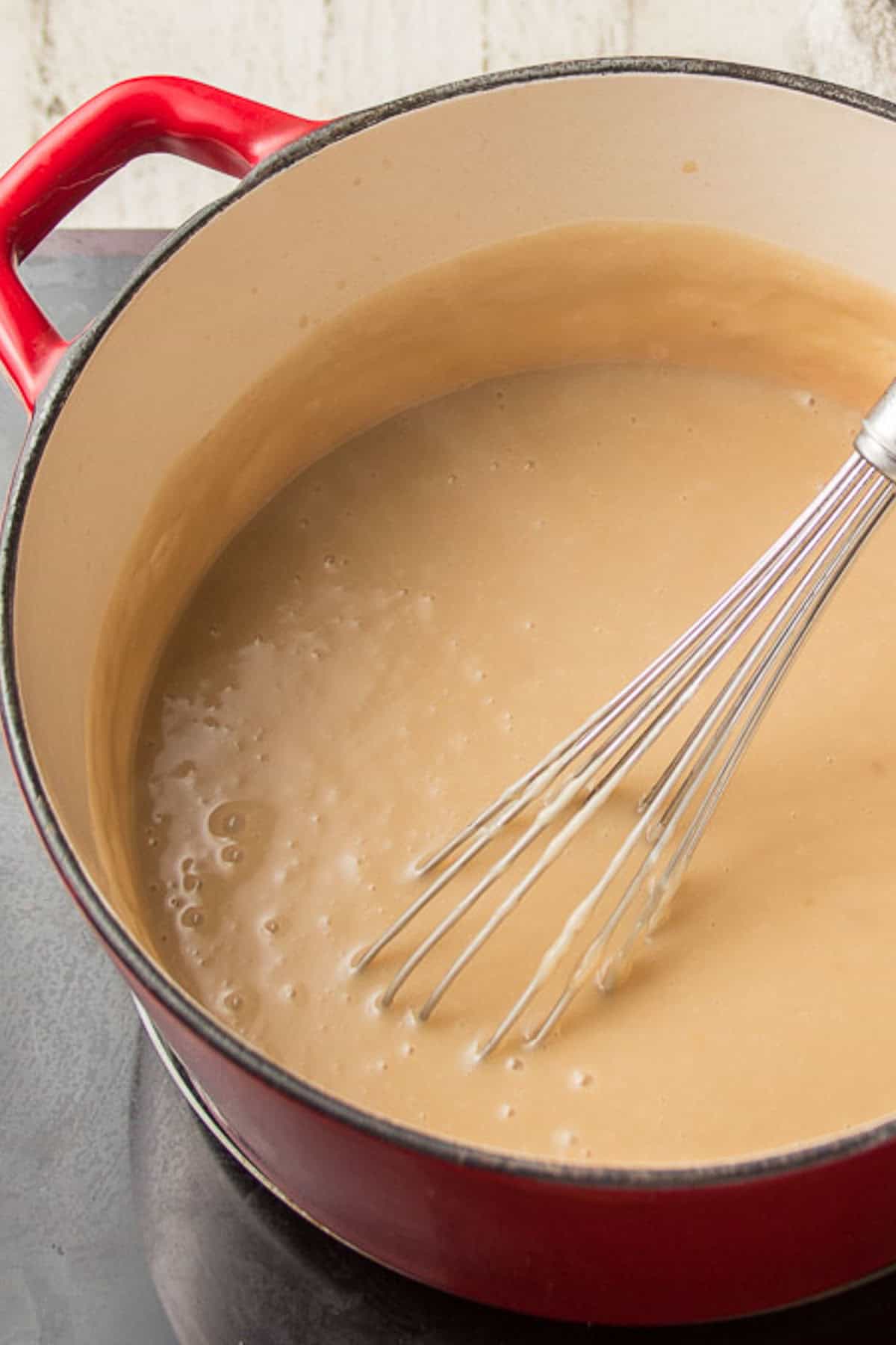 Vegan butterscotch pudding in a pot with wire whisk.