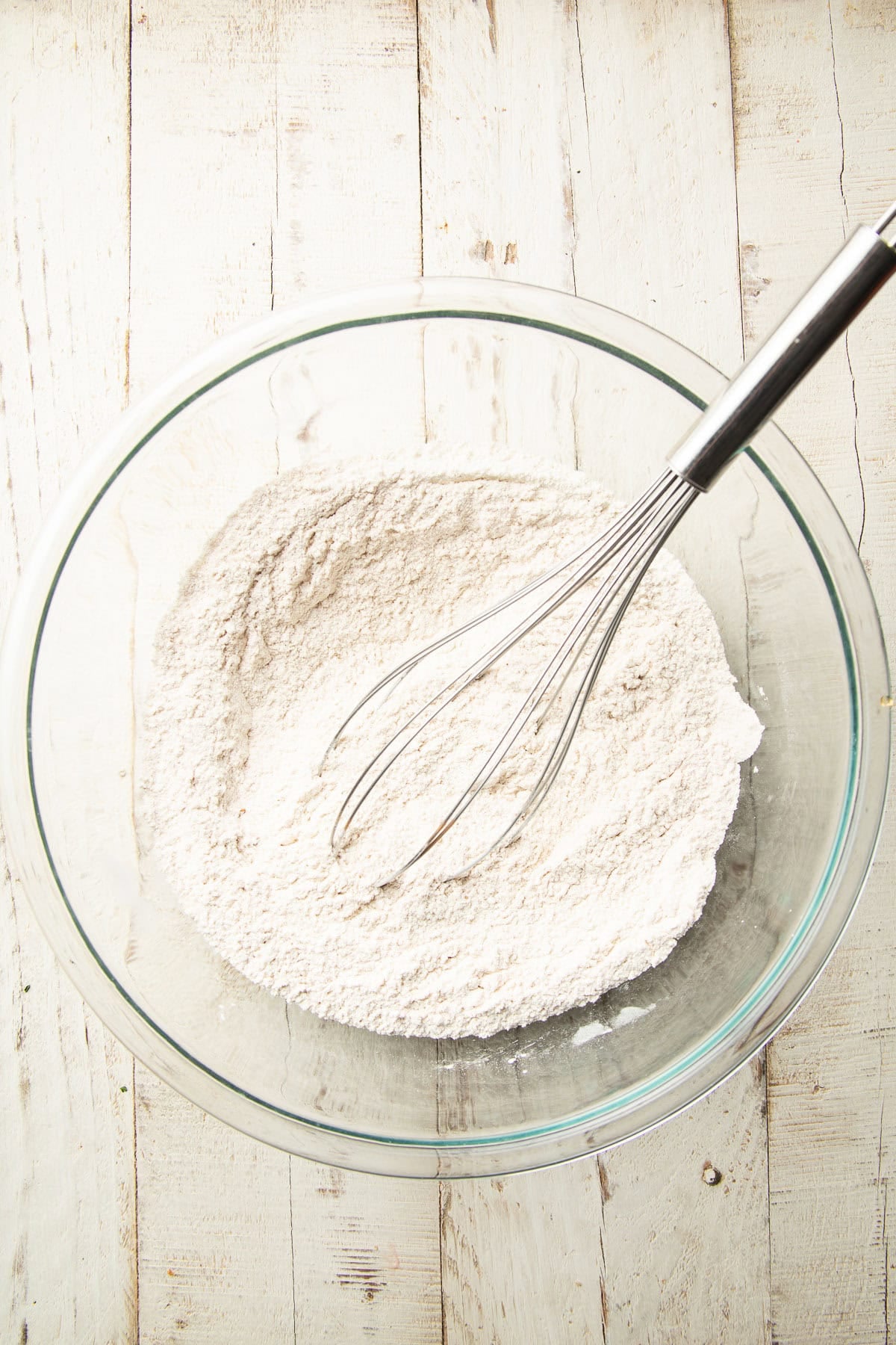 Dry ingredients for cake in a mixing bowl with wire whisk.