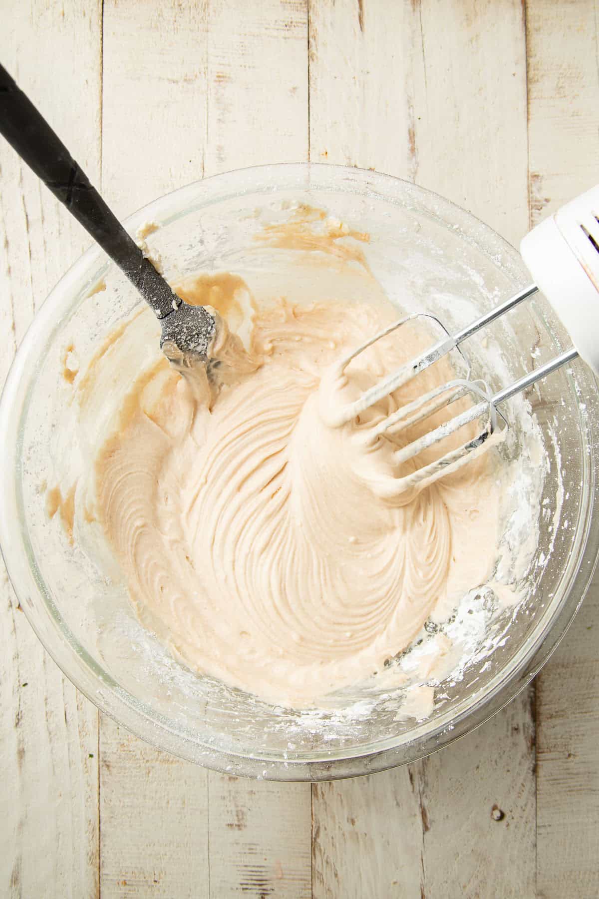 Vegan cinnamon cream cheese frosting in a mixing bowl with electric mixer and spatula.