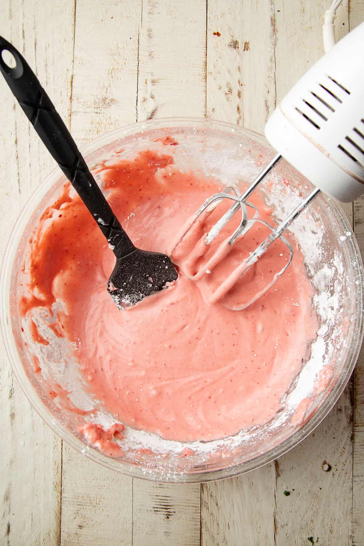Vegan strawberry cream cheese frosting in a mixing bowl with electric mixer and spatula.
