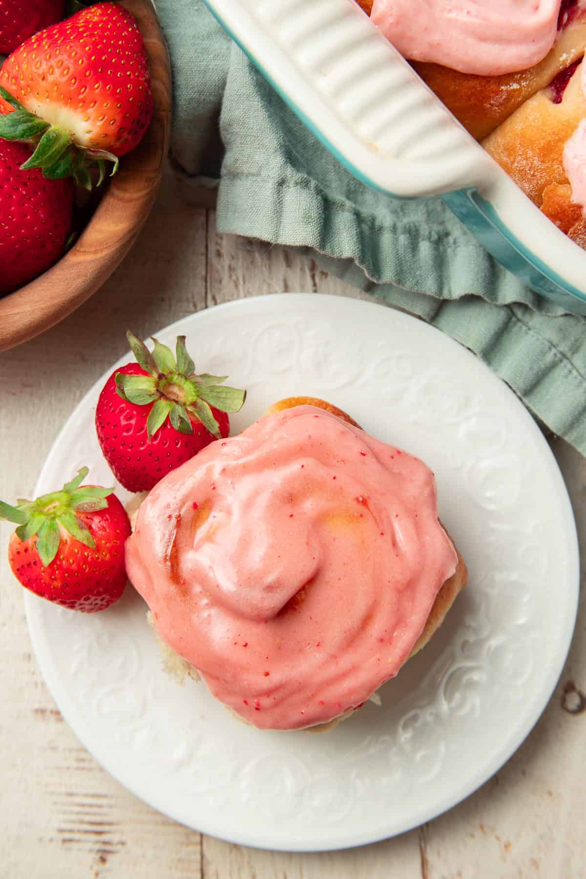 White wooden surface set with Vegan Strawberry Roll on a plate and bowl of strawberries.