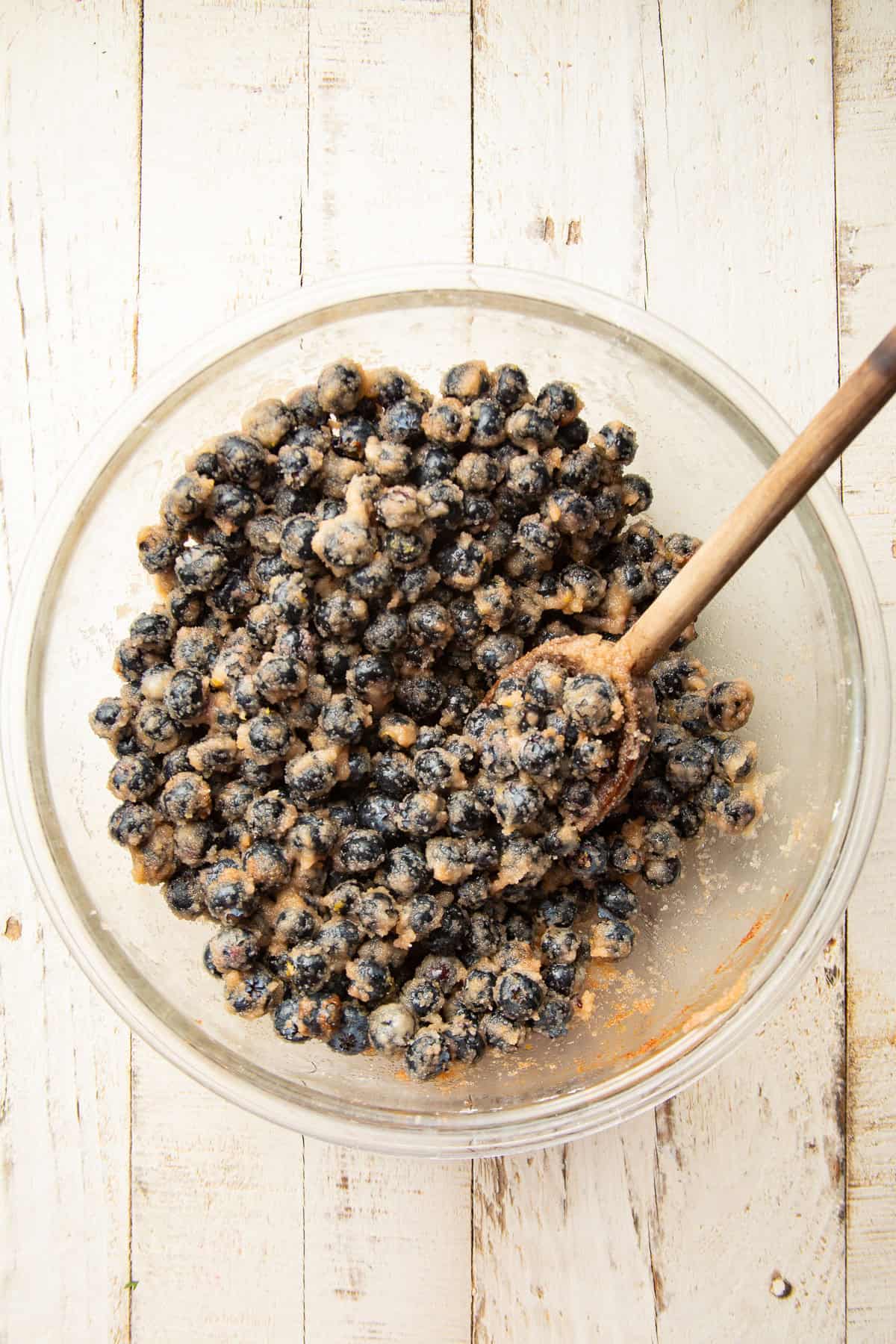 Glass bowl filled with raw blueberry pie filling with wooden spoon.