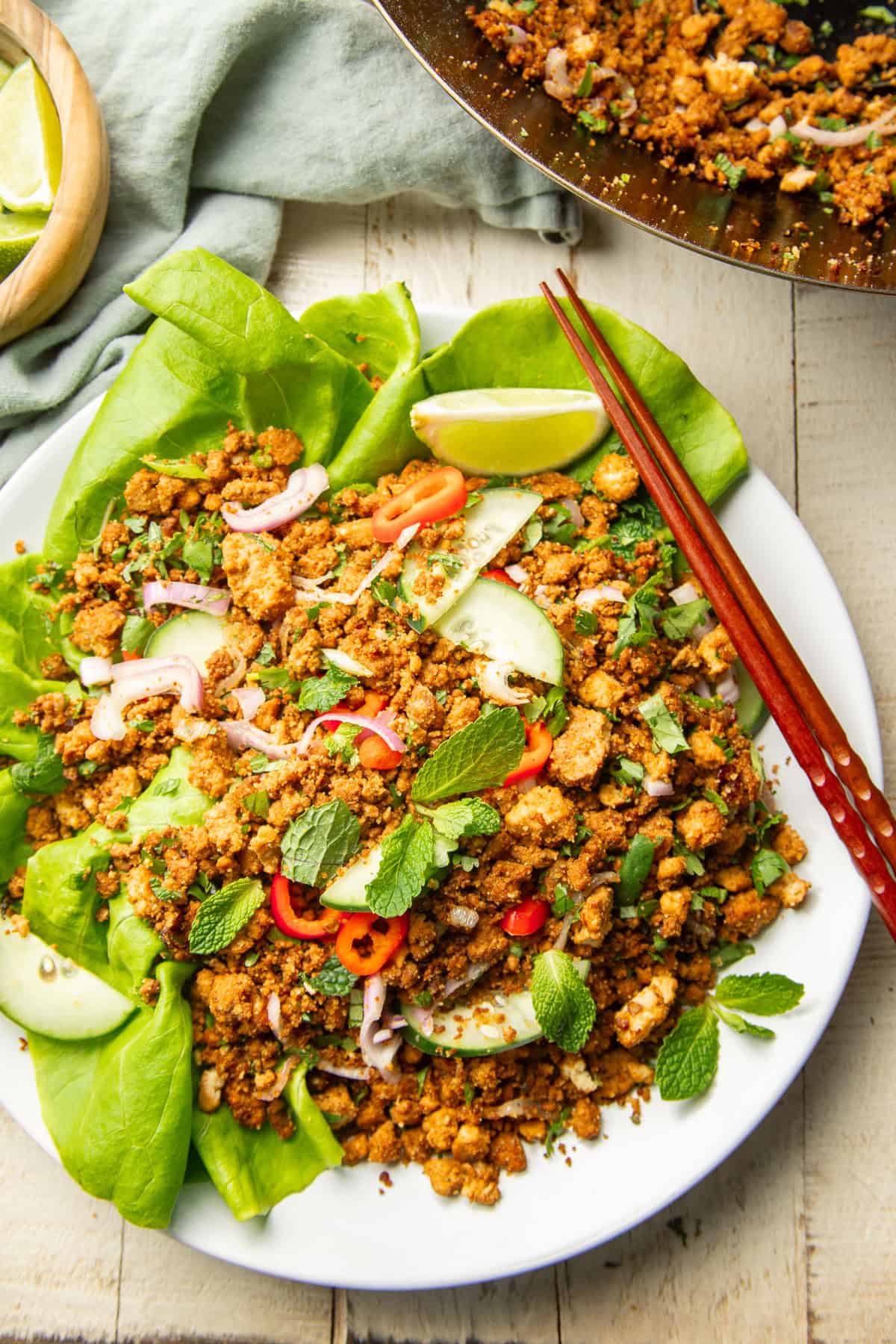 White wooden surface set with a wok and plate of Vegan Larb.