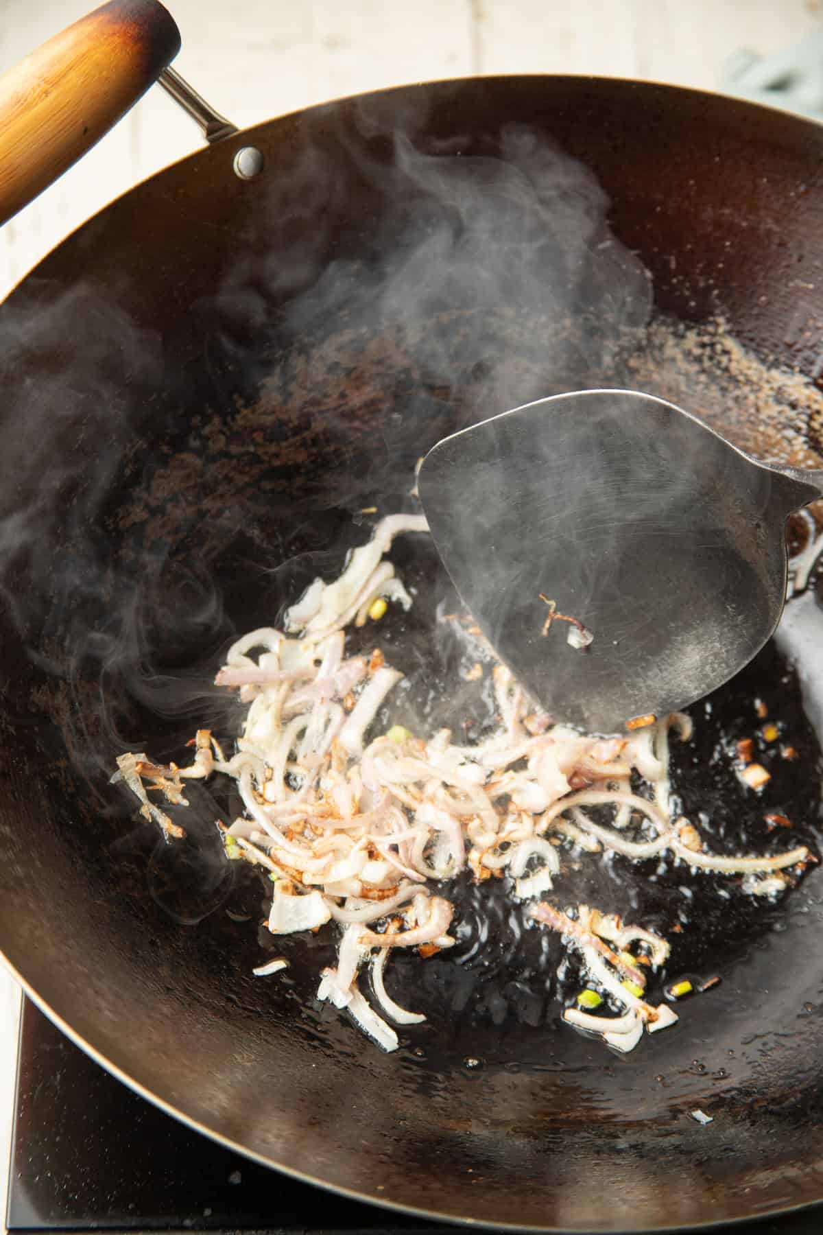 Sliced shallots cooking in oil in a wok.