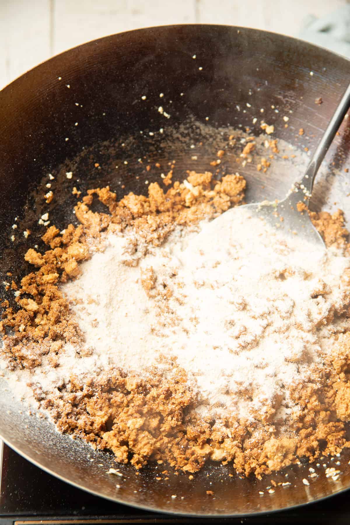 Crumbled tofu in a wok with toasted jasmine rice powder.