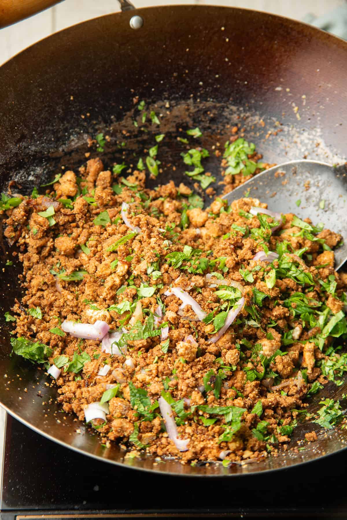 Vegan Larb in a wok with sliced shallots and fresh herbs.