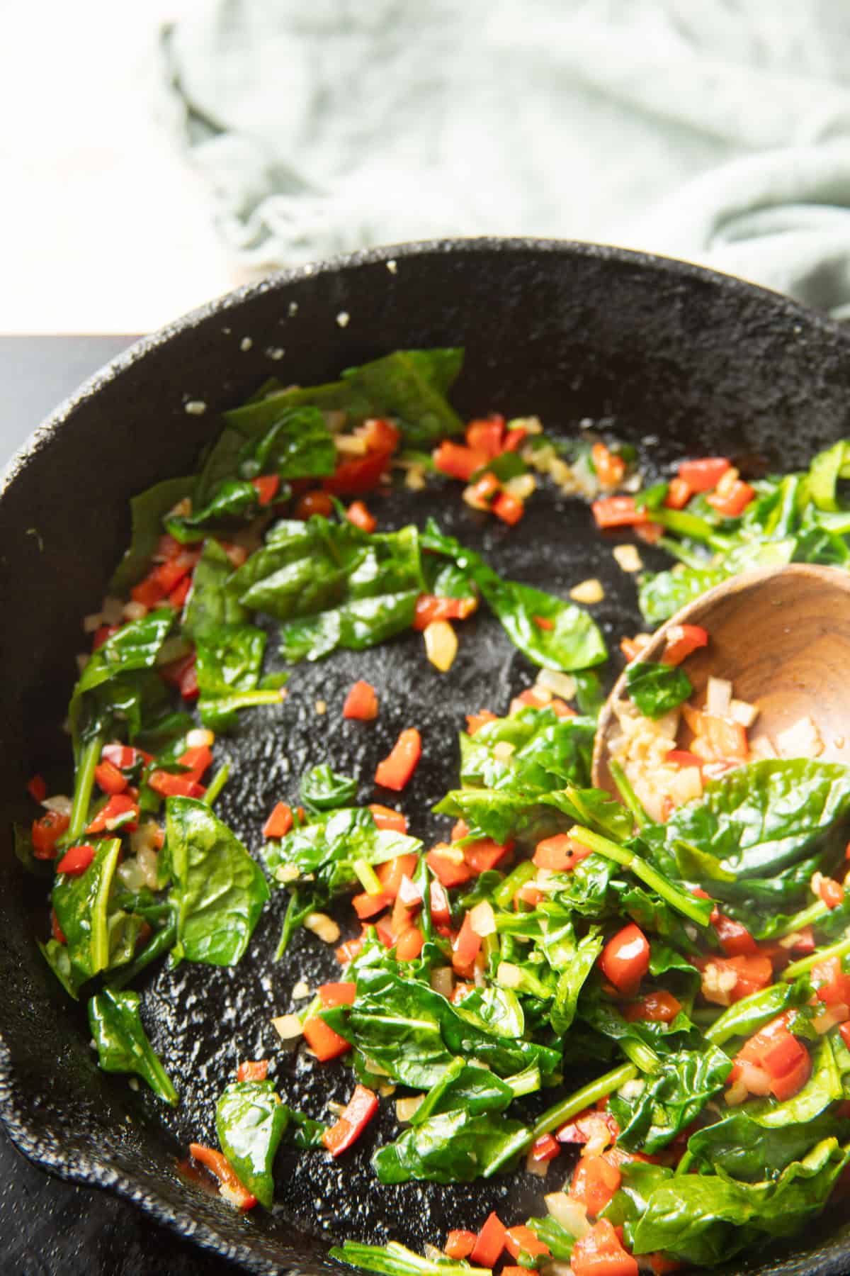 Mixture of spinach, diced peppers, and diced onion cooking in a skillet.