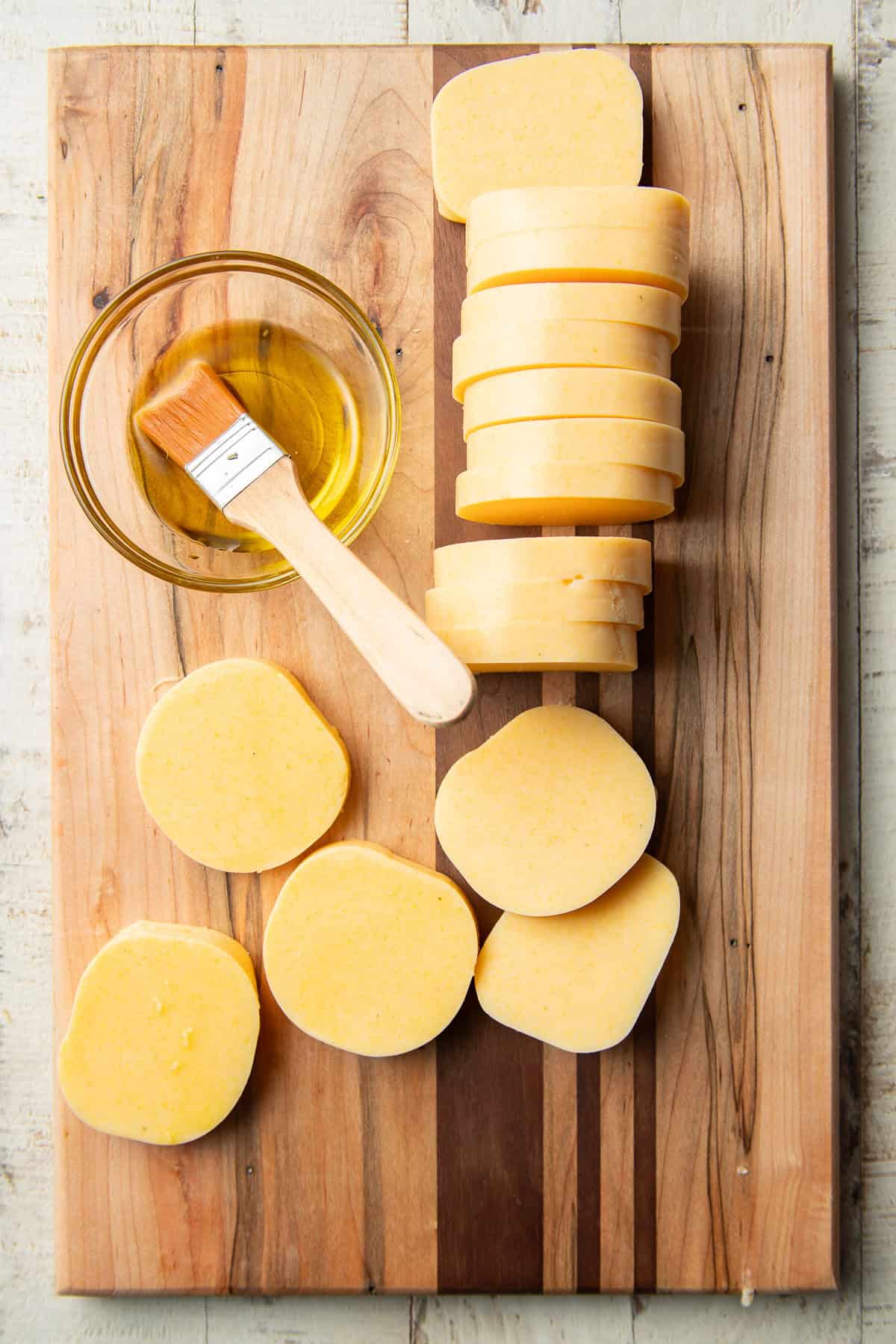 Sliced tube of polenta and bowl of olive oil on a cutting board.