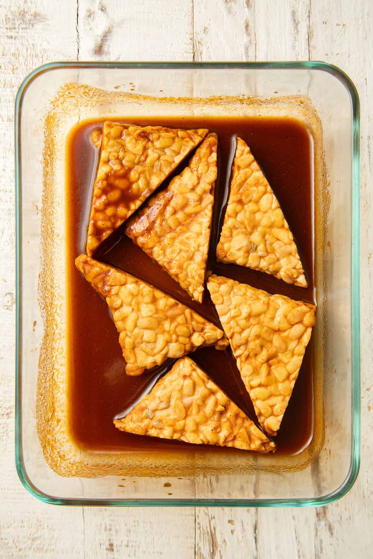 Tempeh triangles soaking in marinade in a dish.