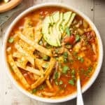 Bowl of Vegan Sopa de Lima topped with tortilla strips and avocado slices.