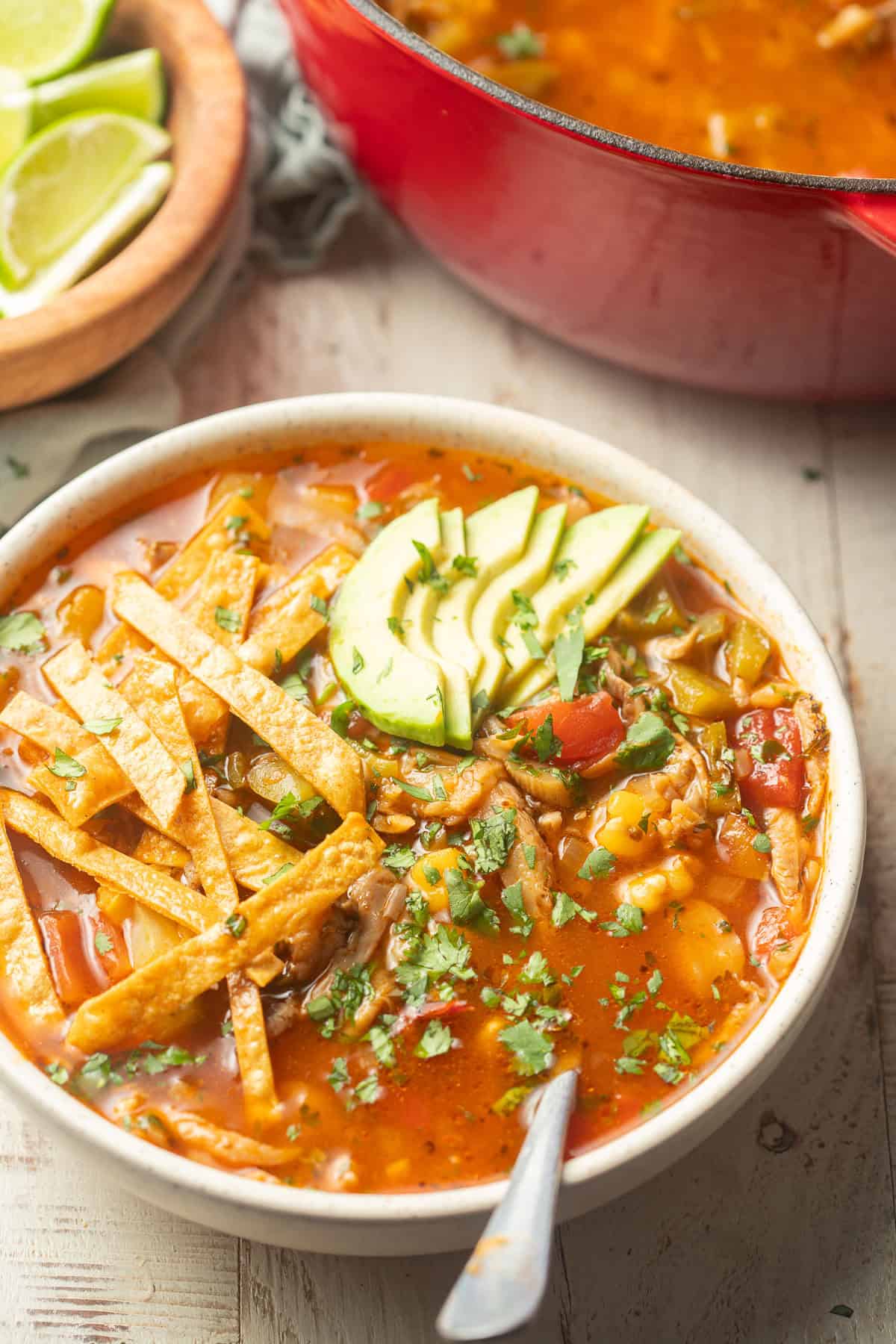 Bowl of Vegan Sopa de Lima with a red pot in the background.