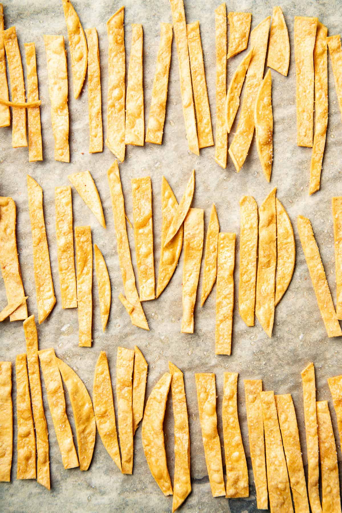 Baked tortilla strips on a parchment paper-lined baking sheet.