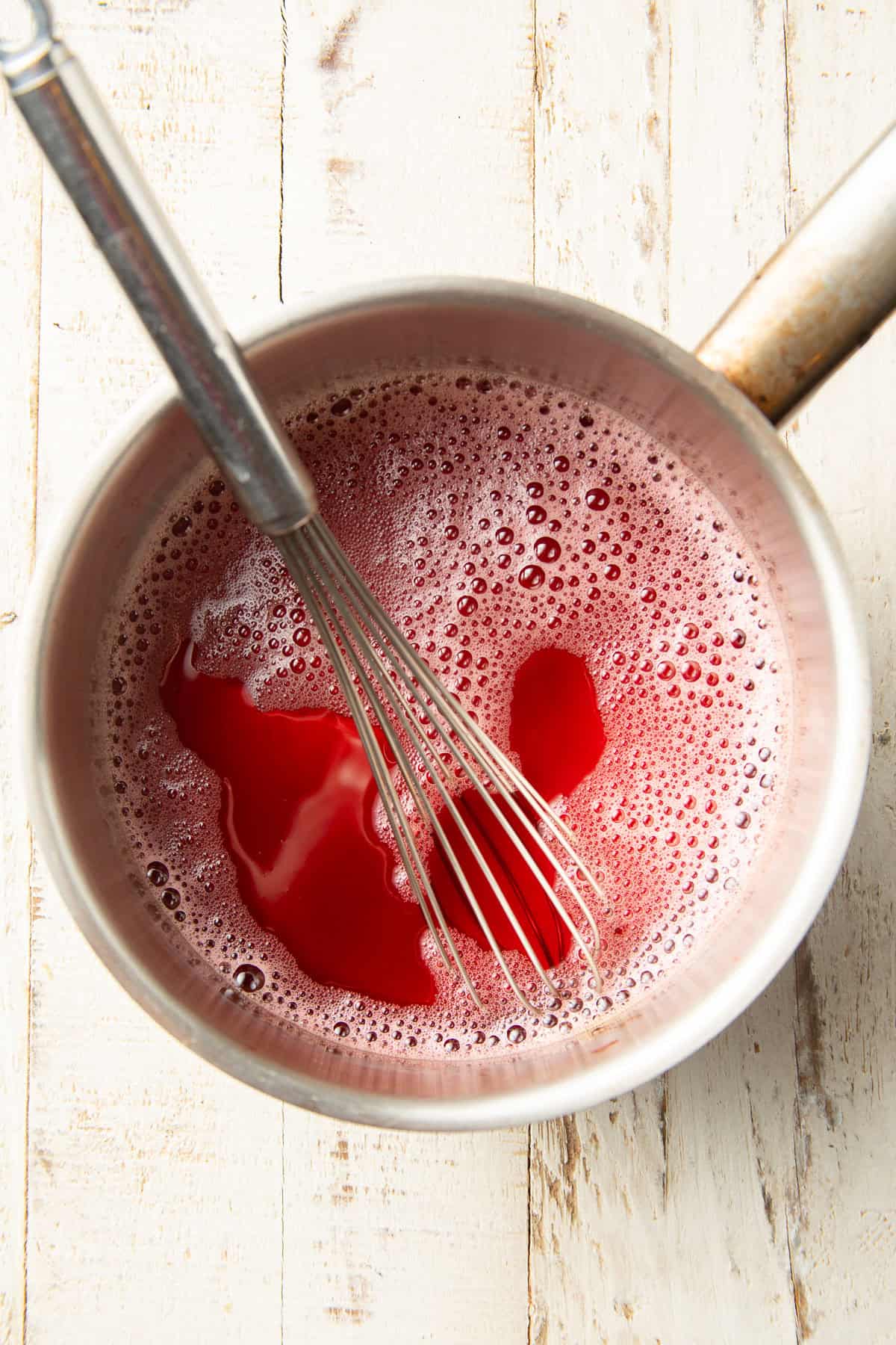 Whisk and saucepan filled with fruit juice.