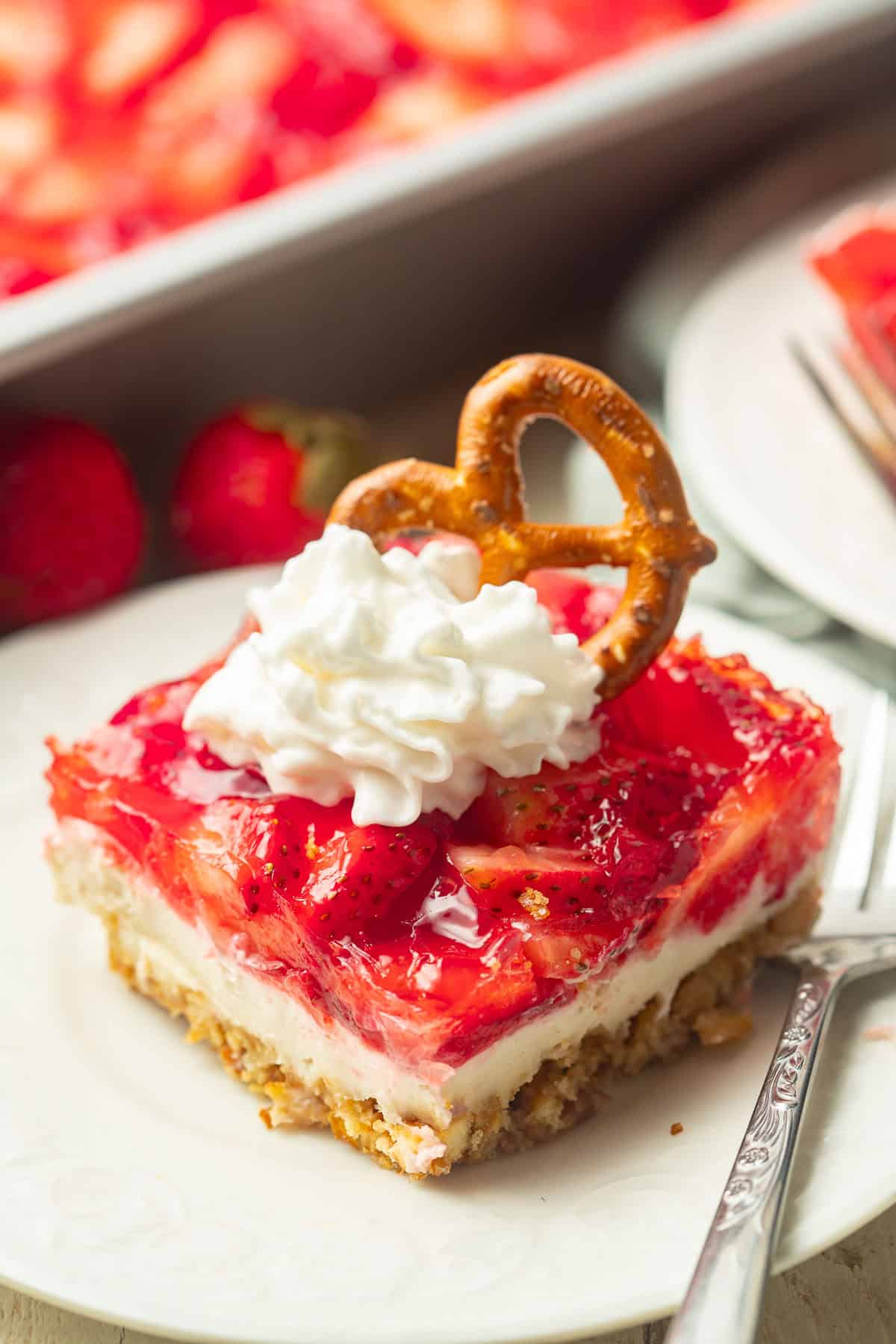 Slice of Vegan Strawberry Pretzel Salad on a plate with baking dish in the background.