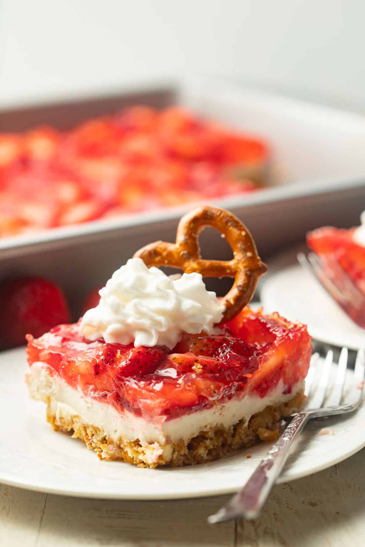Slice of Vegan Strawberry Pretzel Salad with whipped cream and mini pretzel on top.