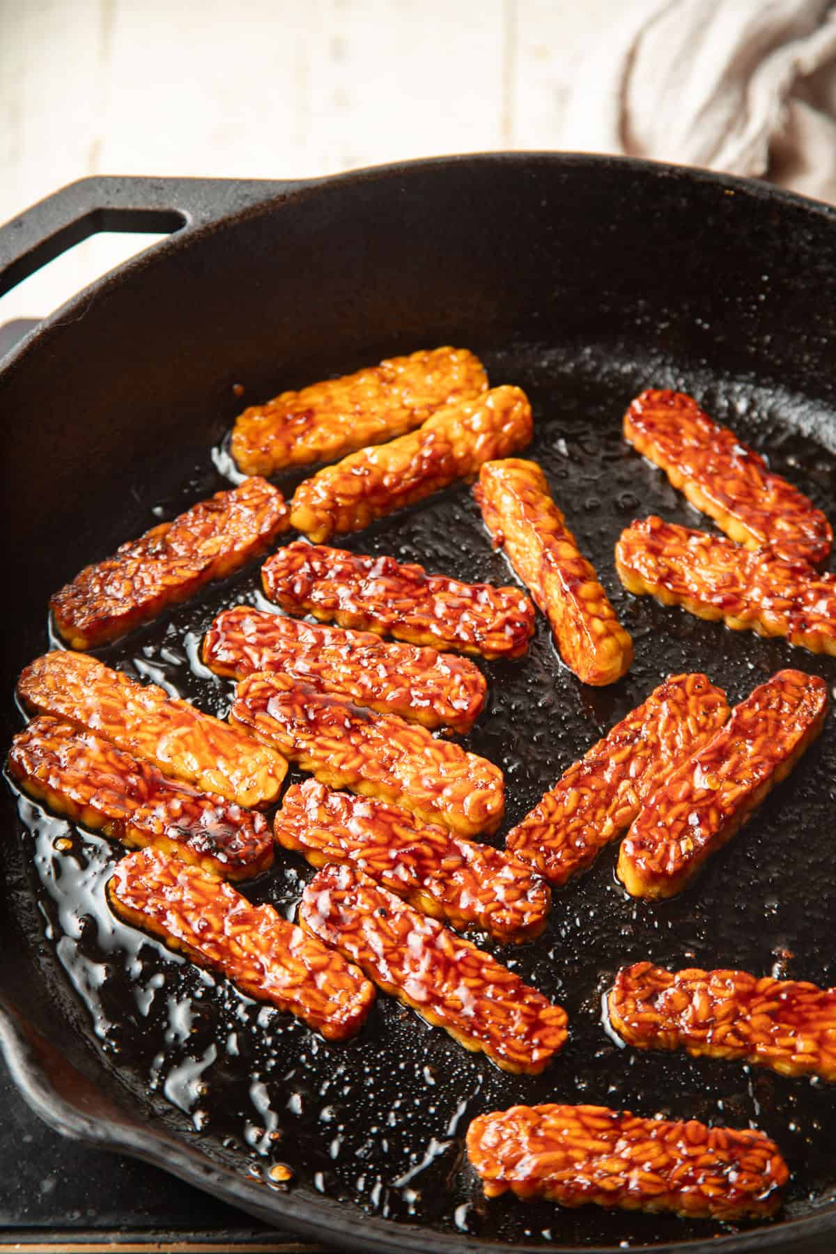 Glazed tempeh strips cooking in a skillet.