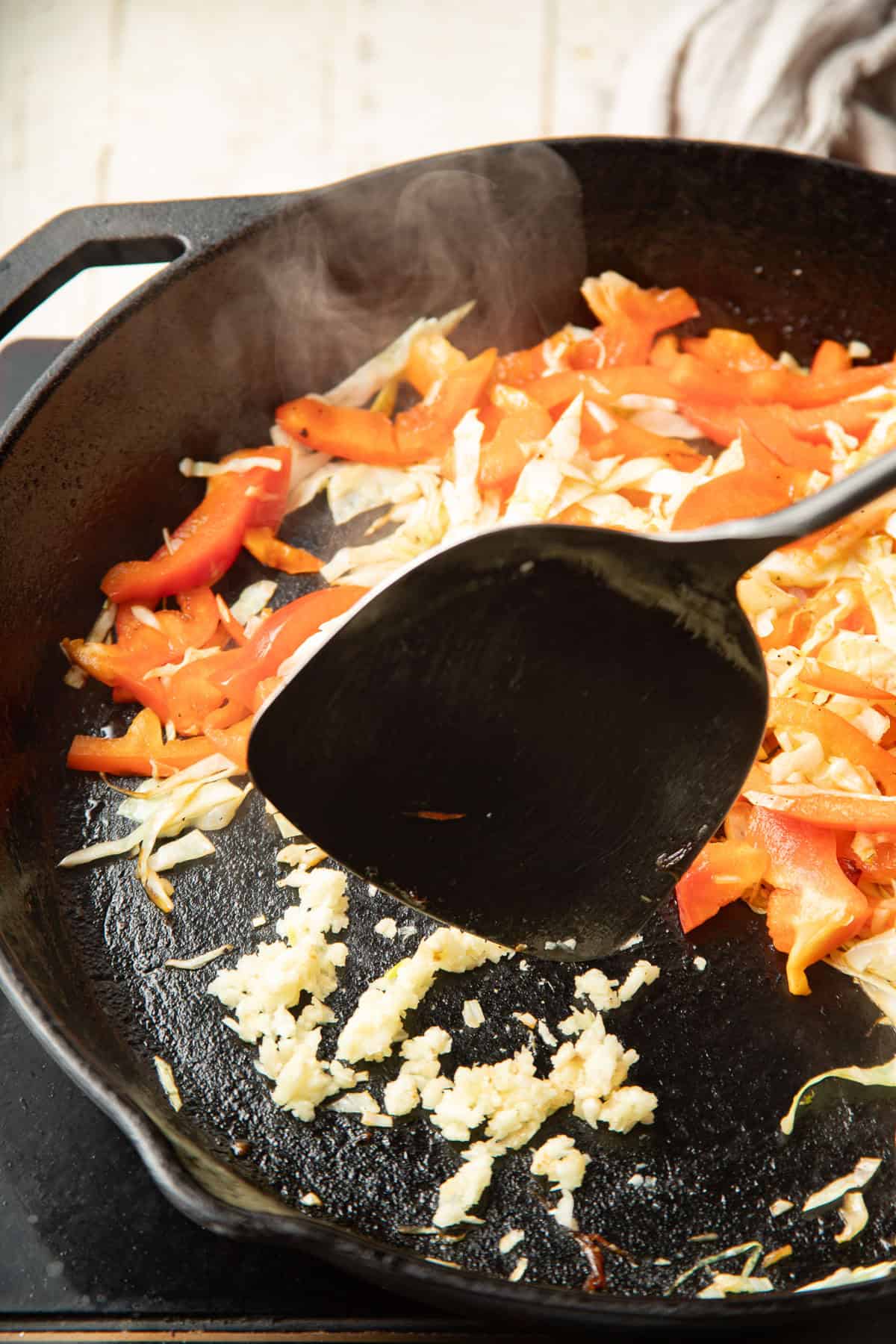 Garlic cooking in a skillet with cabbage and peppers.