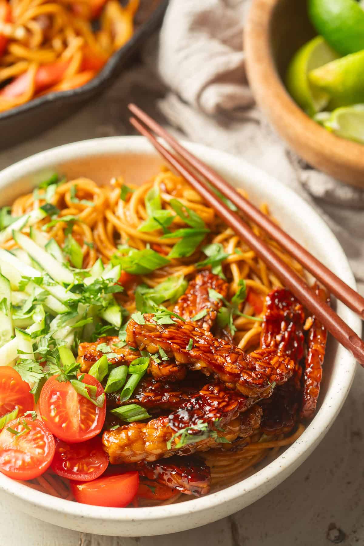 Tempeh Noodle Bowl with bowl of limes and skillet in the background.