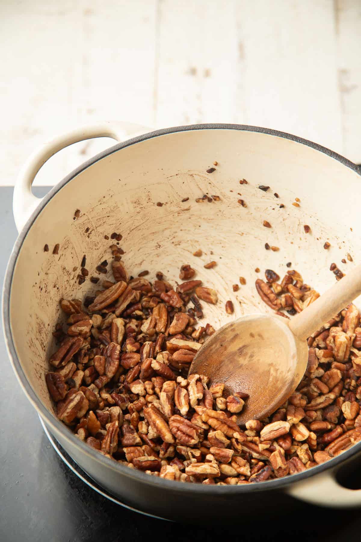 Chopped pecans and butter cooking in a pot with wooden spoon.