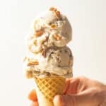 Hand holding cone with two scoops of Vegan Butter Pecan Ice Cream.