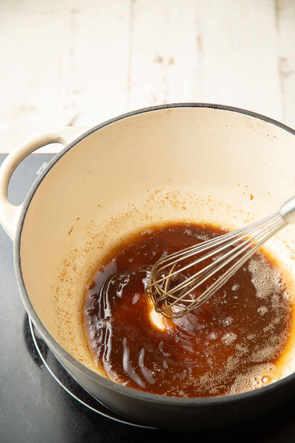 Brown sugar and vegan butter cooking in a pot with wire whisk.