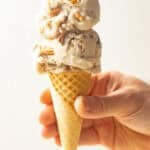 Hand holding a cone with two scoops of Vegan Butter Pecan Ice Cream.