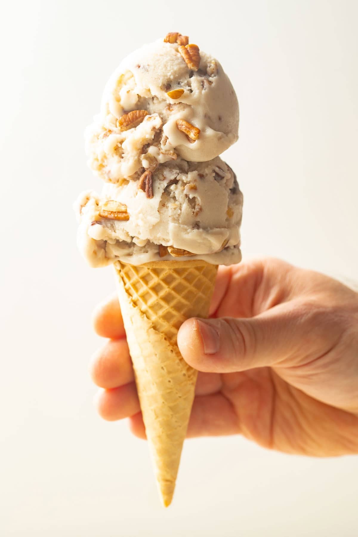 Hand holding a cone with two scoops of Vegan Butter Pecan Ice Cream.