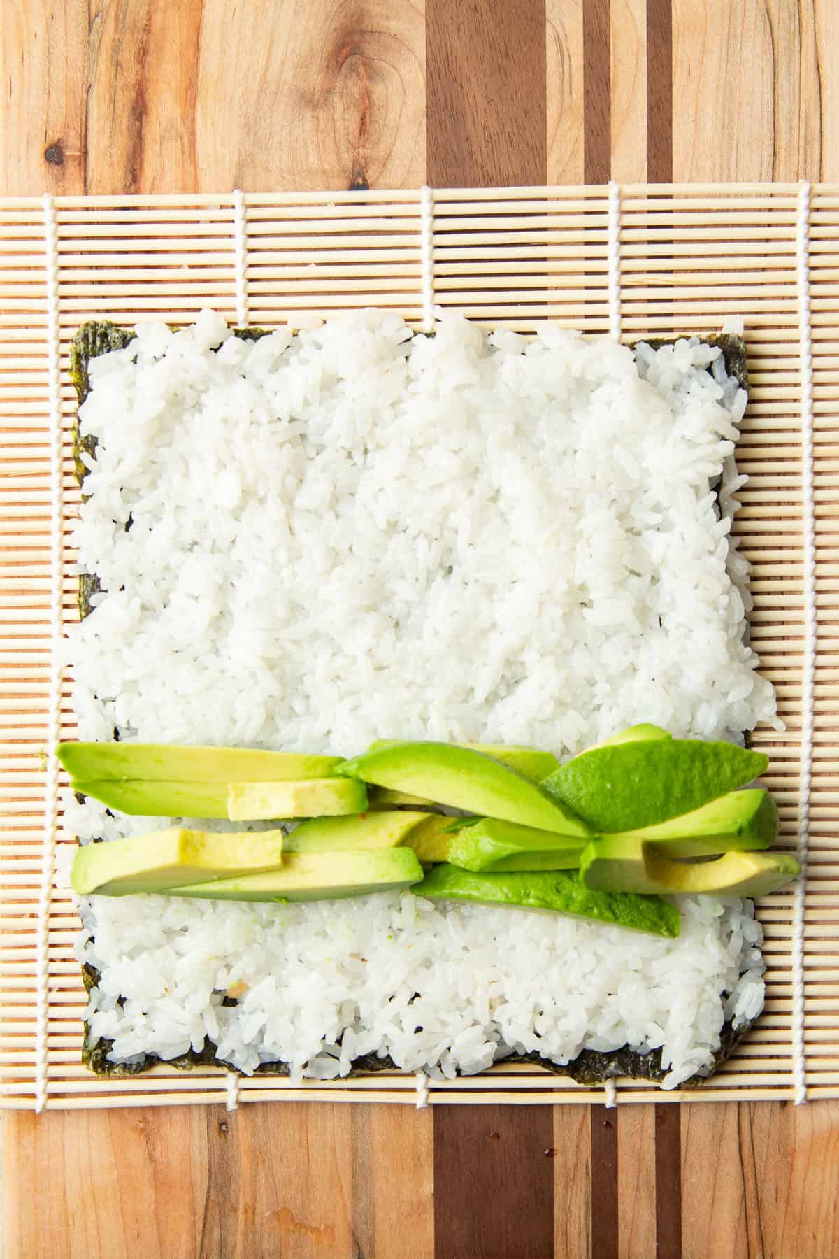 Nori sheet covered with rice and a strip of avocado slices.