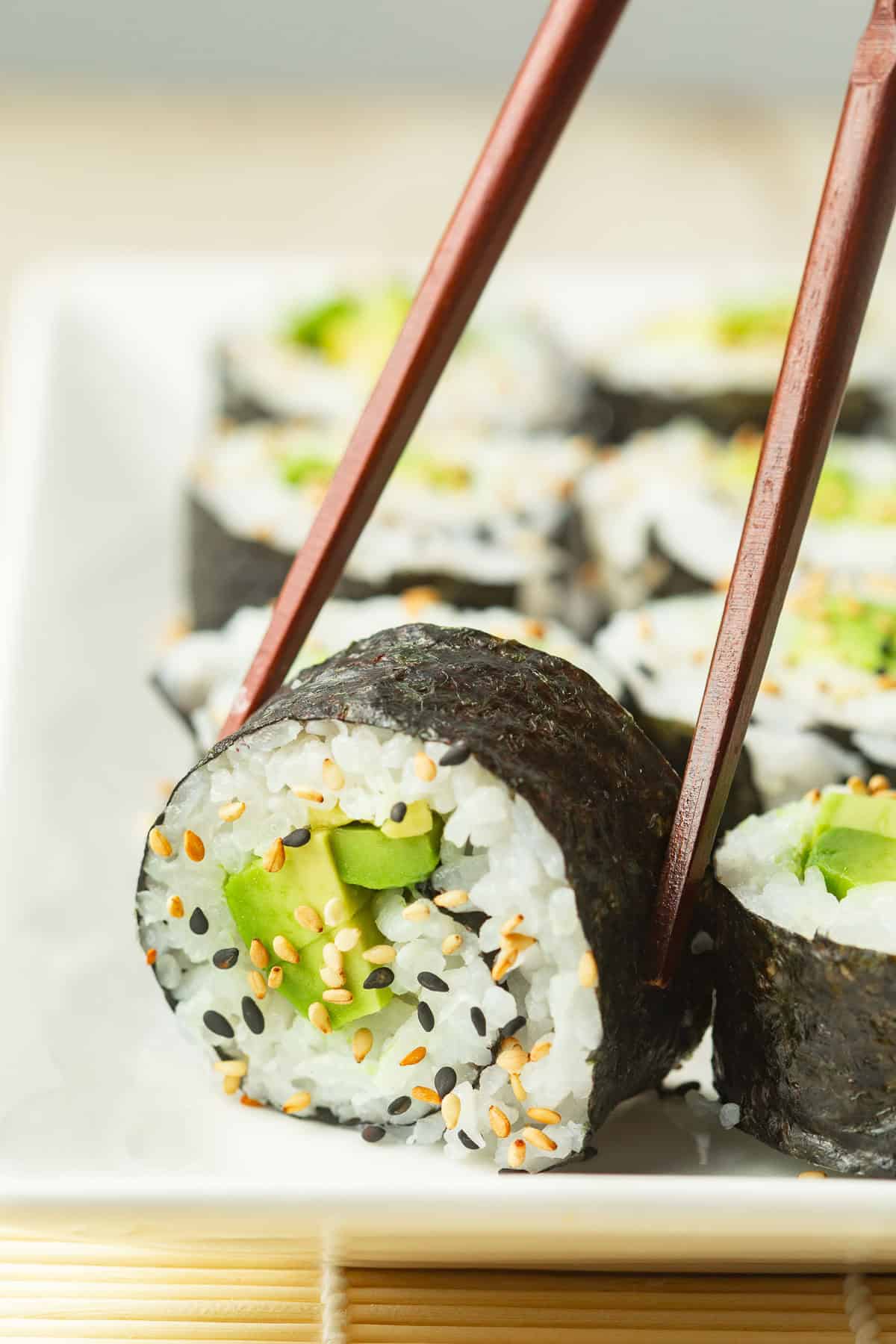 Chopsticks picking up a piece of Avocado Sushi from a dish.