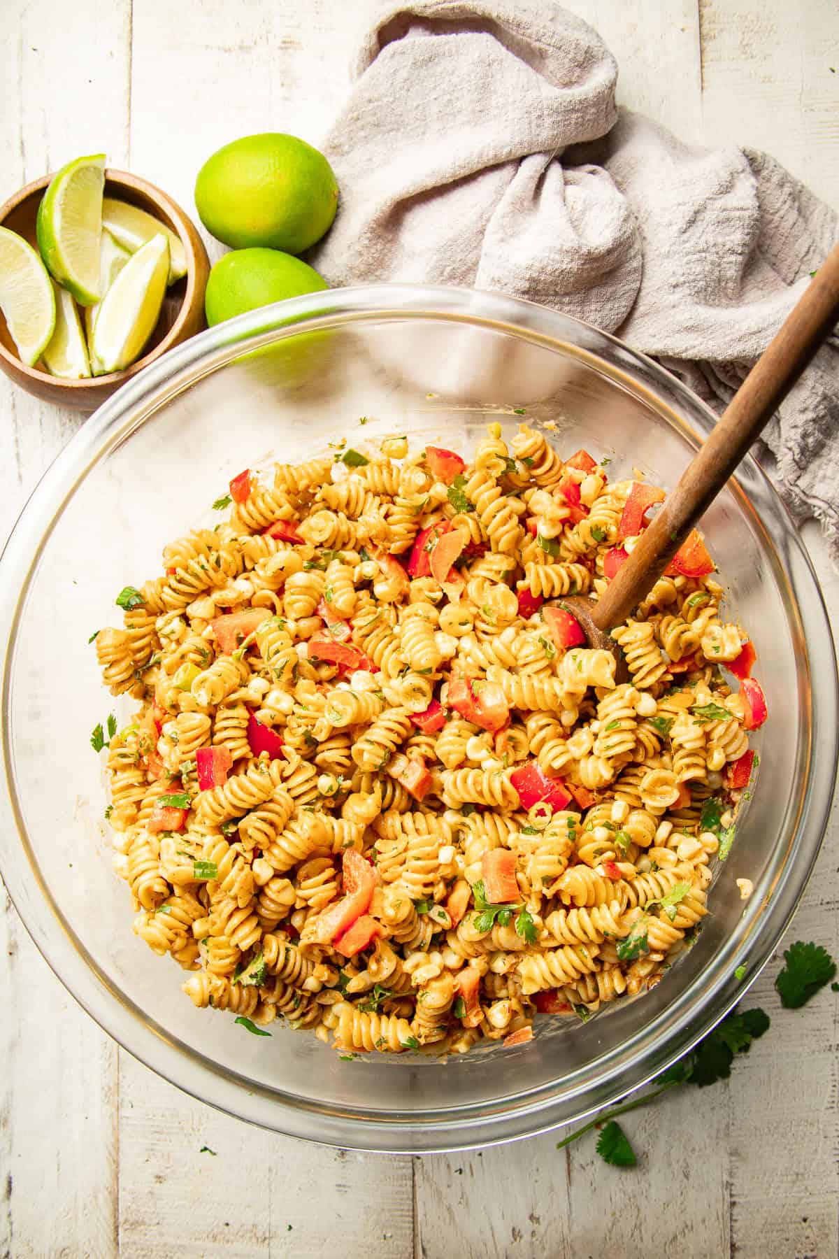 White wooden surface set with a bowl of Street Corn Pasta Salad, napkin, and limes.