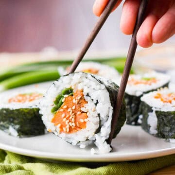 Hand with chopsticks picking up a piece of Sweet Potato Sushi from a plate.