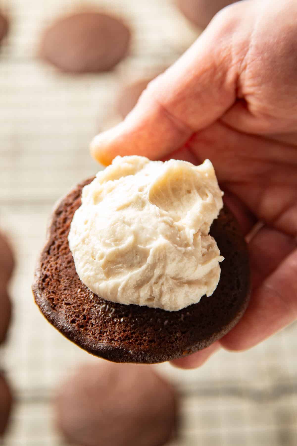 Hand holding half a vegan whoopie pie with filling on top.