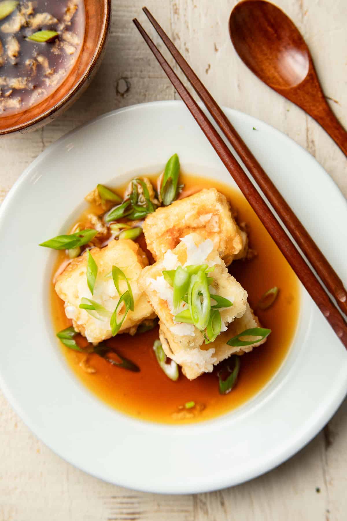 Vegan Agedashi Tofu cubes on a plate with chopsticks and spoon on the side.