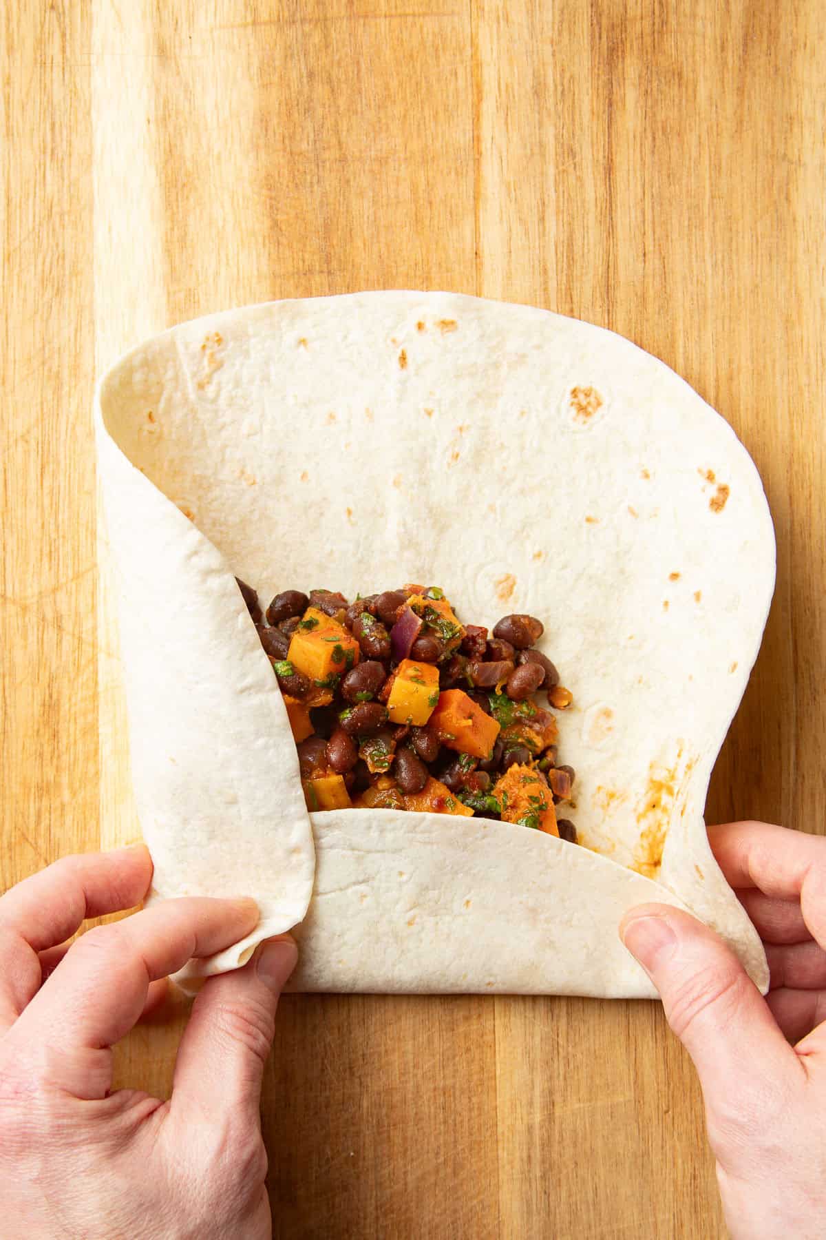 Hands wrapping butternut squash black bean filling in a flour tortilla.