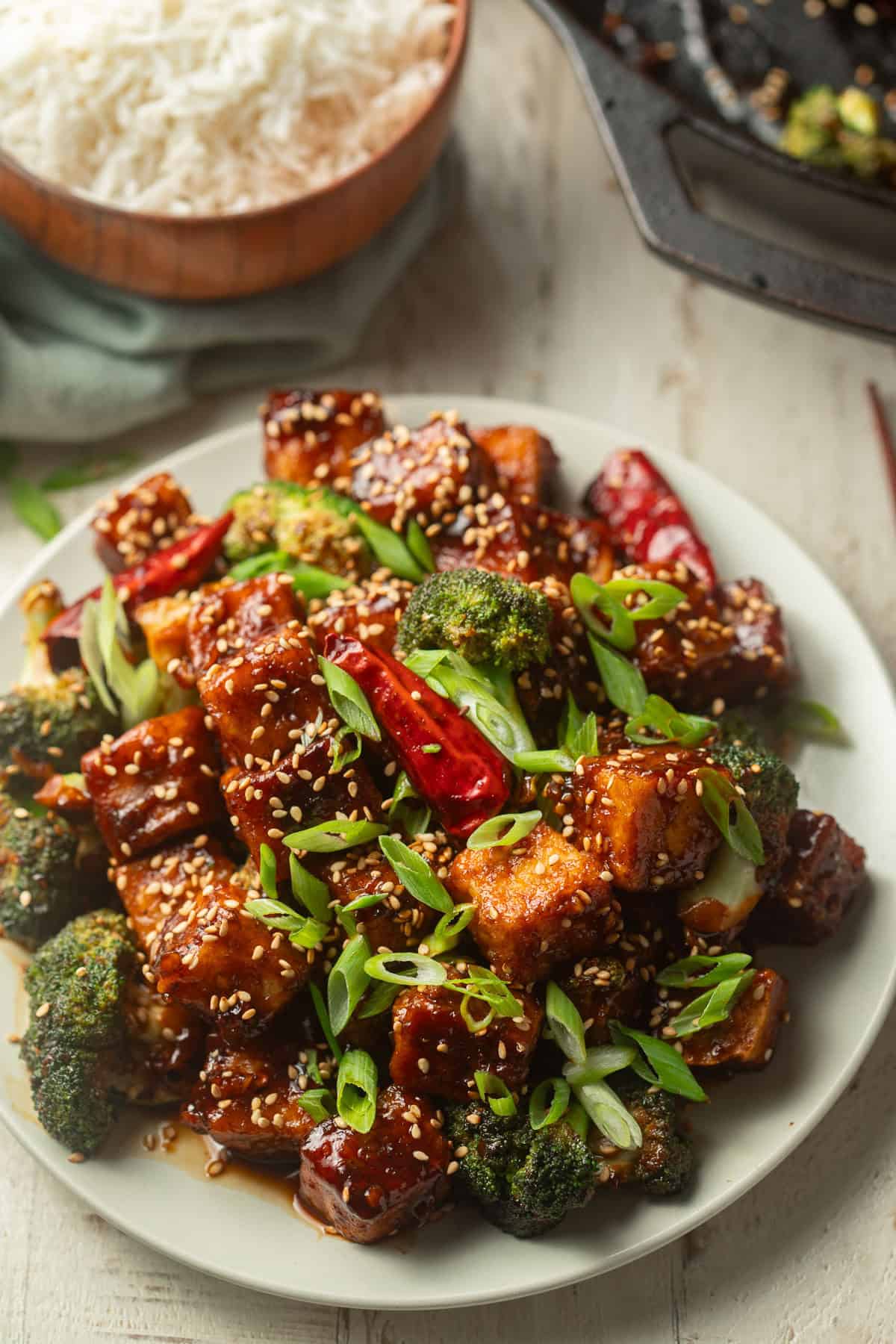 Plate of General Tso's Tofu with skillet and bowl of rice in the background.